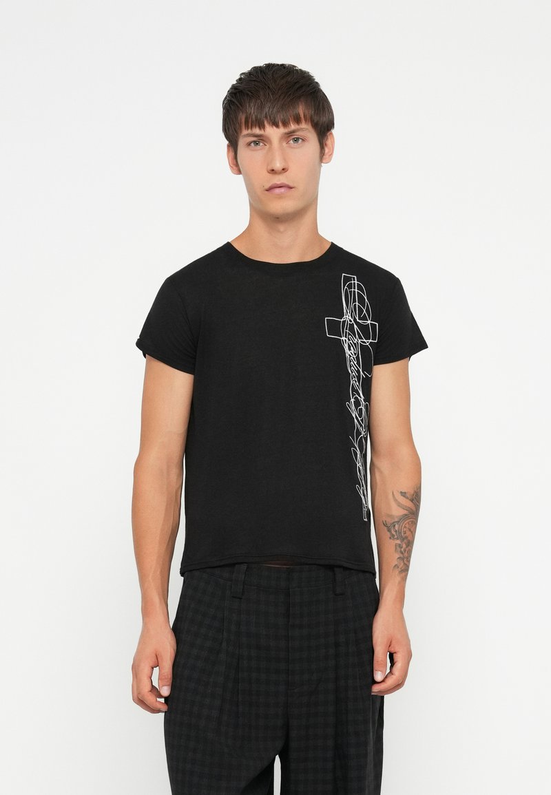 Czarny bawełniany t-shirt z krótkim rękawem, z białym abstrakcyjnym wzorem po lewej stronie. Model w ciemnych, kraciastych spodniach.