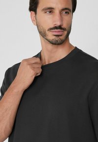 T-shirt noir à manches courtes avec un col rond. Tissu doux et lisse avec une coupe régulière, mettant en avant un détail de couture subtil au niveau de l'encolure.