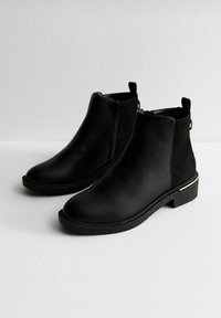 Botines negros de tobillo hechos de cuero liso; cuentan con un cierre lateral, punta redondeada, tacón bajo y un sutil acento dorado en el tacón.