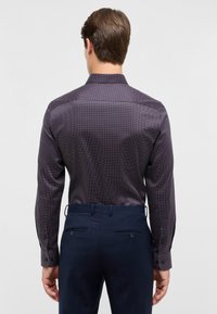 Camicia a maniche lunghe di colore viola scuro con piccoli pois bianchi e rossi, forma aderente, dettaglio della spalla sul retro e polsini con bottoni.