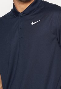 Marinblå polo med slät tyg, med en klassisk krage, två knappar och en vit Nike-logga på bröstet.