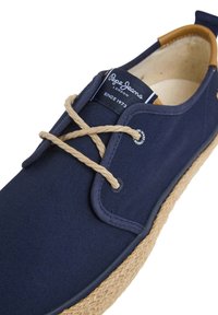 Scarpa in tela navy con suola in corda naturale, dotata di lacci beige, occhielli metallici rotondi e un'etichetta con il logo sulla linguetta.