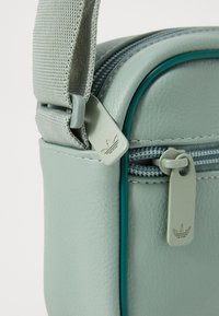 Borsa a tracolla sintetica verde chiaro con finitura texturizzata, dotata di chiusura con zip, dettagli in verde petrolio e tirazip con logo.