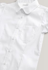 Bela majica s kratkimi rokavi iz gladke tkanine ima ovratnik, zapenjanje na gumbe in en žep na prsnem delu z zaobljenimi robovi.