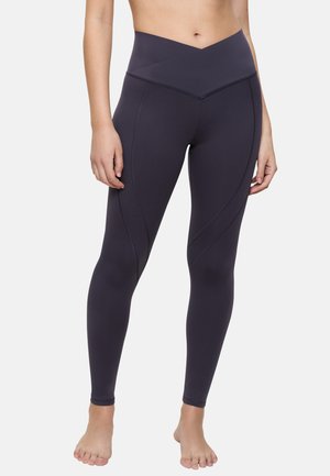 Hoch sitzende, dunkelviolette Leggings aus elastischem Material, mit einem Zickzackmuster und kontrastierenden Nähten an den Seiten.