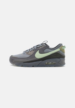 Seitenansicht eines grauen Nike Air Max Sneakers mit hellgrünem Swoosh, Obermaterial aus Mesh und Wildleder, durchsichtiger Sohle und sichtbarer Luftdämpfungseinheit.