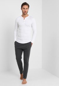 Witte lange mouwen henley shirt met drie knopen bij de hals, gecombineerd met donkergrijze, taps toelopende sweatpants. Soepele stof met minimale textuur.