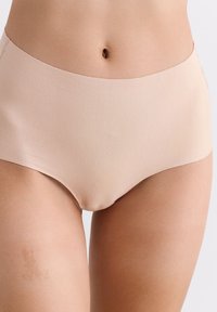 Close-up van een persoon die naadloze, huidskleurige, hoge tailleonderbroek draagt, met zichtbare buik en bovenbenen.