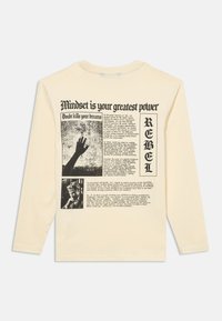Beżowa koszula z długim rękawem z czarnym tekstem i grafiką, w tym "Mindset is your greatest power", uniesioną dłonią, osobą i napisem "REBEL".