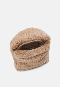 Sac beige en peluche, fabriqué dans un matériau moelleux, avec une ouverture douce et surdimensionnée et une doublure en tissu lisse comportant une petite étiquette à l'intérieur.