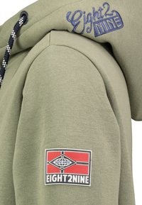 Olijfgroene hoodie met een trekkoord, voorzien van blauwe geborduurde branding en een patchlogo in rood en zwart op de linker mouw.