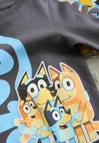 Grå sweatshirt med et livligt cartoon-print af animerede hunde, med klare farver og tydelige karaktertræk. Blødt, behageligt stof.