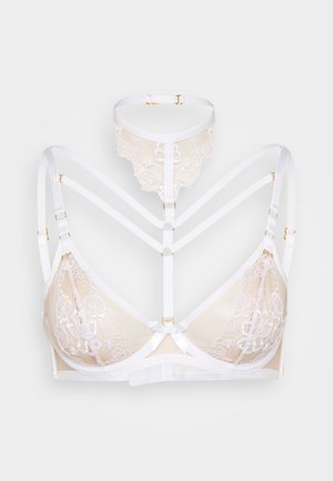 Bralette en dentelle et mesh beige avec bretelles blanches. Comprend des éléments en métal doré, des motifs floraux et un nœud central. Design à lanières.