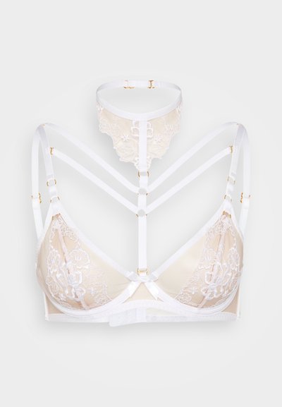 Krajková a síťovaná podprsenka v béžové barvě s bílými ramínky. Má zlaté kovové doplňky, květinové vzory a střední mašličku. Design s pásky.
