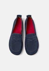 Zapatos de ante azul marino tipo slip-on con punta redonda, que presentan un detalle de costura en el empeine y un forro interior de un rojo brillante.