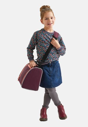 Sac violet avec des accents de fermeture éclair orange, taille enfant, design doux et arrondi. L'enfant porte un pull à motifs floraux, une jupe en jean et des leggings gris.