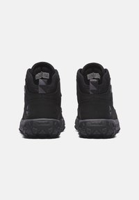 Černé vysoké tenisky s texturovaným svrškem z kůže a síťoviny, vyznačující se gumovou podrážkou s hrubým vzorkem. Logo Timberland na boku.