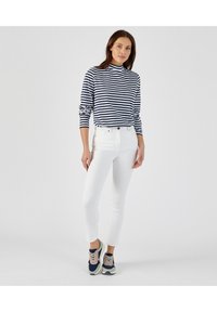 Gestreepte langemouwen top in marineblauw en wit, gecombineerd met strakke witte jeans en multicolore sneakers met blauwe, roze en groene accenten.
