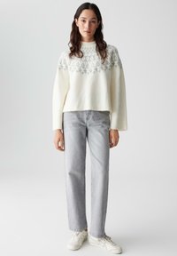 Maglione bianco a maglia con una giacca grigia a motivo, abbinato a jeans dritti grigio chiaro e sneakers bianche. Tessuto morbido e vestibilità comoda.