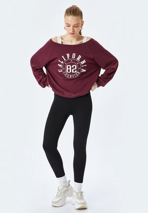 Bordeaux oversized sweatshirt med hvid "California 82" grafik, parret med sorte leggings og beige sneakers. Enkel design med ribbede manchetter.