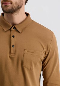 Bruine polo met lange mouwen en een kraag, voorzien van drie zwarte knopen, een borstzak en geborduurde branding op de zak.