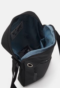 Borsa in tessuto nero con apertura a zip, dotata di una fodera interna blu e una piccola tasca frontale. Include una tracolla e dettagli in occhioletto metallico.