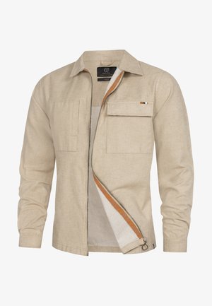 Beige långärmad skjorta i texturerad väv, med två framfickor, en orange dragkedja och en liten dekorativ lappar med ränder.