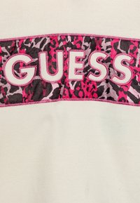 Vit sweatshirt med en djärv "GUESS"-logotyp i vitt med rosa kontur och ett flerfärgat djurmönster i rosa, svart och grått.