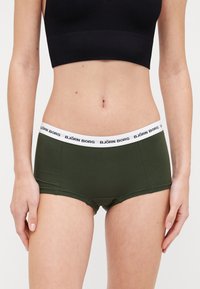 Boyshorts verdi realizzati in morbido tessuto elasticizzato con una vita elastica bianca caratterizzata da testo nero del marchio, design aderente per il comfort.
