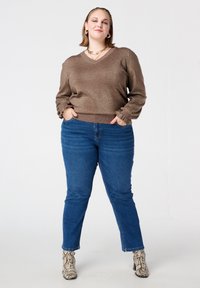 Bronzen, glinsterende trui met V-hals en gerimpelde manchetten, gecombineerd met blauwe spijkerbroek, aangevuld met enkellaarsjes met slangenprint.