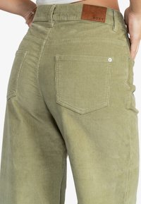 Groene corduroybroek met een hoge taille, voorzien van twee achterzakken, een leren logo-opdruk en een zachte textuur.