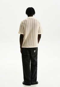 Cream vertical striped knit top with short sleeves, paired with loose black jeans featuring back pockets and a label. Smooth texture.