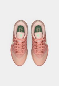 Pastelsed roosad spordijalatsid valge logoga ja rohelise sisetallaga, vaadatuna ülalt valgel taustal.