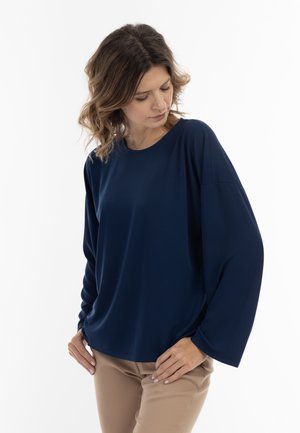 Marineblaues Langarmshirt mit lockerer Passform, rundem Halsausschnitt und weicher Textur, kombiniert mit hellbeigen Hosen. Glattes, minimalistisches Design.