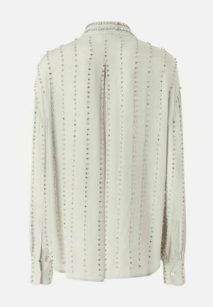 Blusa beige chiaro a maniche lunghe con file verticali di piccoli borchie argento, polsini con bottoni e piega centrale sulla schiena.