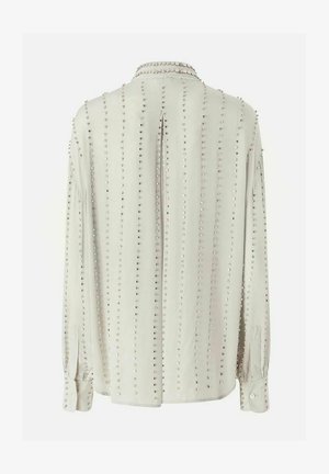 Blusa beige chiaro a maniche lunghe con file verticali di piccoli borchie argento, polsini con bottoni e piega centrale sulla schiena.