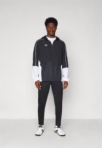 Sort og hvid hættejakke med lynlås, elastisk talje og frontlomme. Kombineret med sorte slim-fit bukser og hvide sneakers.