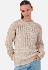 Pull en tricot couleur crème avec un motif texturé en forme de vagues, col rond, poignets et ourlet côtelés. Associé à un jean bleu clair.