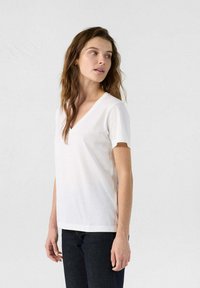 T-shirt bianco in cotone con scollatura a V e maniche corte, caratterizzato da una texture morbida e una vestibilità comoda. Indossato con jeans scuri.