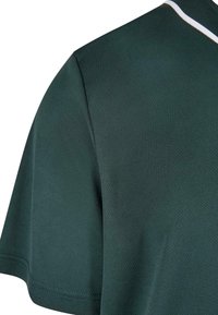 Section de chemise à manches courtes texturée vert foncé avec un détail de col rayé blanc et bleu sur un fond blanc uni.