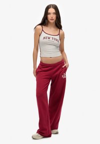 Grauer Cropped-Top mit bordeauxrotem Saum, auf dem "NEW YORK"-Text steht, kombiniert mit locker sitzenden, langen bordeauxroten Sweatpants, die ein Logo am linken Bein zeigen.