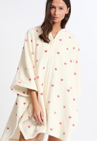 Poncho cappotto in morbido peluche color crema con cappuccio e zip, decorato con motivo di cuoricini rosa sparsi. La texture soffice e le maniche ampie garantiscono comfort e calore.