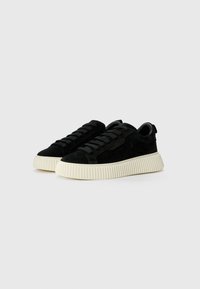 Low-top black suede sneakers with thick ribbed white rubber soles and black laces on plain gray background.