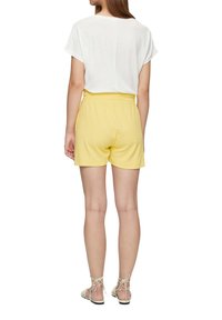 Haut blanc à manches courtes associé à un short jaune à taille élastique et des sandales légères, mettant en valeur un design décontracté et confortable.