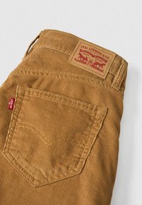 Pantalon en velours côtelé marron avec une poche arrière, l'étiquette rouge Levi's et un patch en cuir de la marque Levi Strauss & Co. au-dessus de la poche.