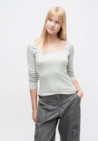 Ανοιχτό γκρι μακρυμάνικο μπλουζάκι με στρογγυλή λαιμόκοψη, εφαρμοστό σώμα και ριμπ υφή, σε συνδυασμό με σκουρογκρί παντελόνι καμπαρντίνα με τσέπες.