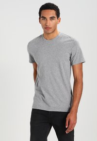 T-shirt grigio in cotone con maniche corte e scollo rotondo. Texture liscia senza motivi o decorazioni visibili, abbinato a jeans scuri.