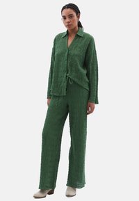 Zelený tkaný dvoudílný set složený z košile s dlouhým rukávem a zapínáním na knoflíky a odpovídajících kalhot širokého střihu s texturovaným vzorem.