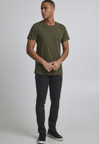 Camiseta a rayas verdes con cuello redondo y un bolsillo en el pecho, combinada con jeans ajustados negros y zapatillas negras con suelas blancas.