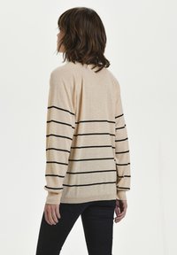 Pull beige rayé avec des lignes horizontales noires, manches longues et coupe décontractée. Texture douce avec poignets et ourlet côtelés.